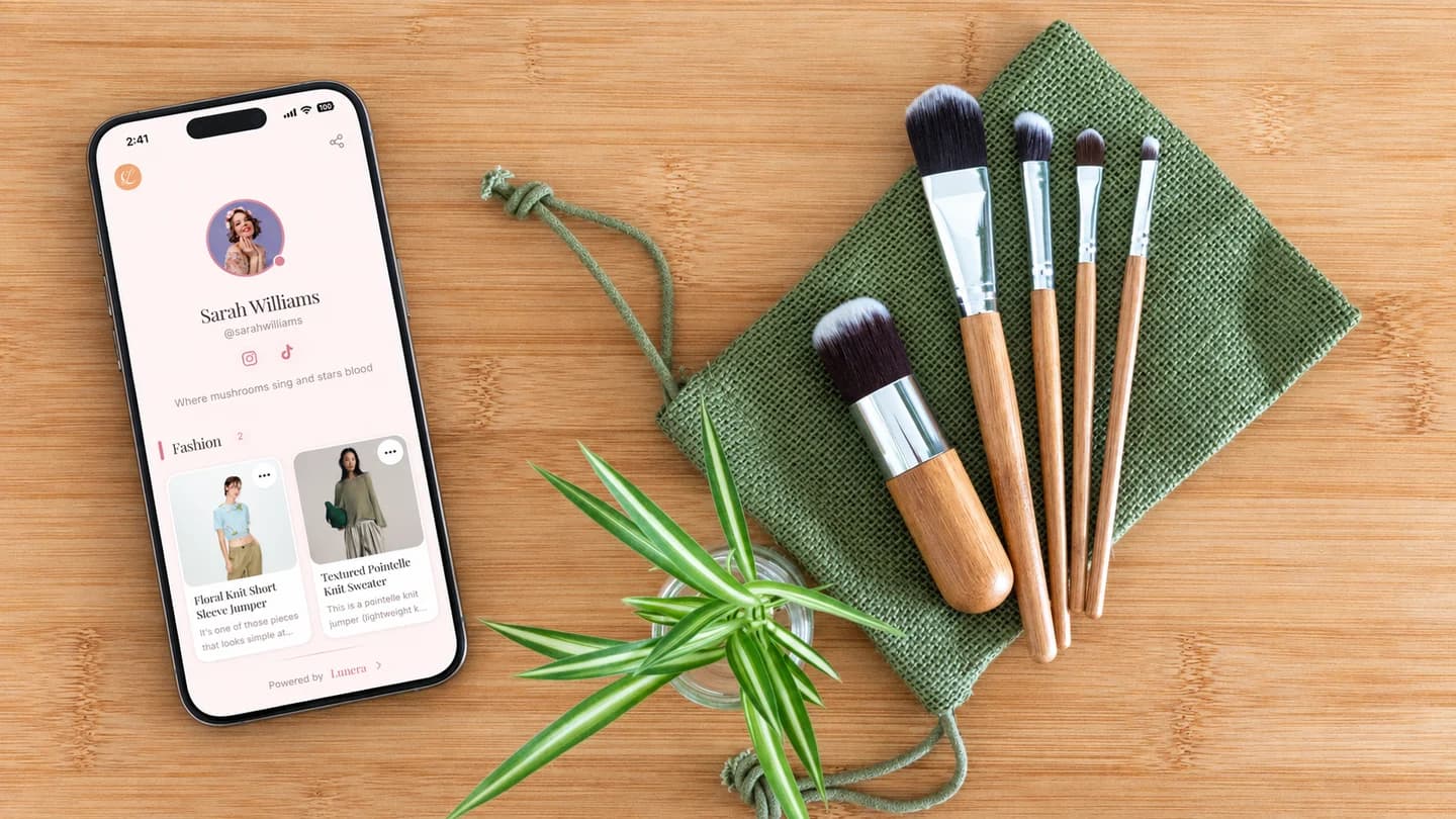 Photo illustration of makeup brushes on wood beside a phone displaying the Lunera profile UI