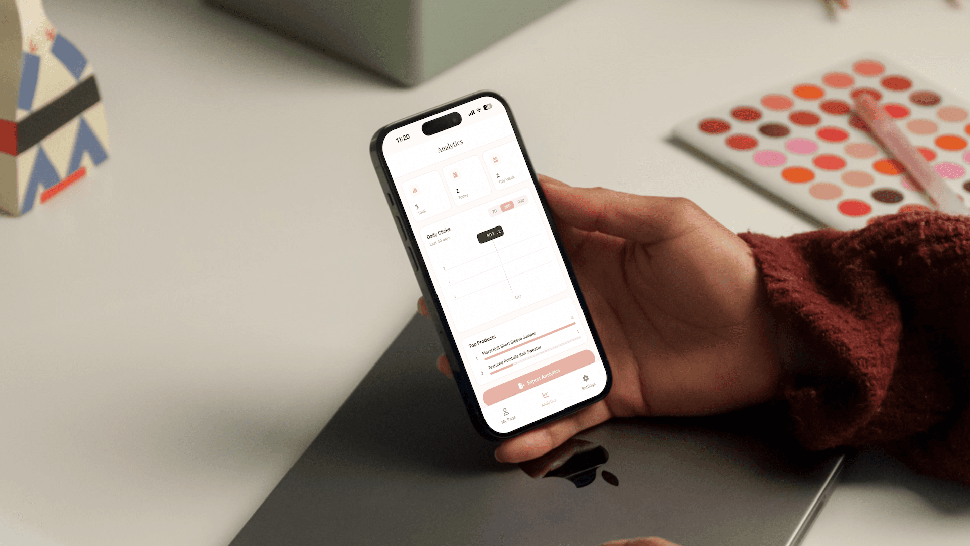 Phone on a desk beside a warm-toned eyeshadow palette and beauty brush